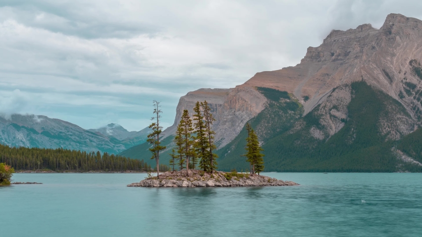 Small island with trees on  Minnewanka lake,a Glacial Lake and the 2nd longest lake in the mountain parks of the Canadian Rockies in Banff Alberta Canada, 4K UHD video, zoom out