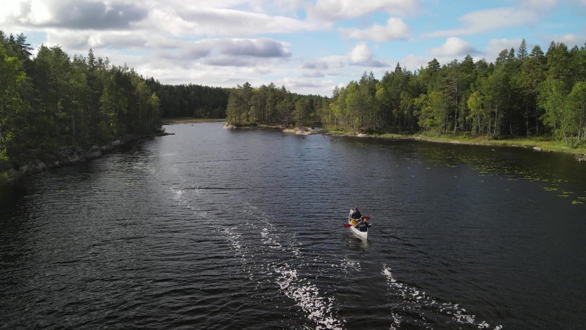 Aerial view of drone flying over Canoers paddling between green pine forest groves on a Swedish lake in Glaskogen nature reserve. Sunny Blue Sky with Clouds with landscape in Sweden