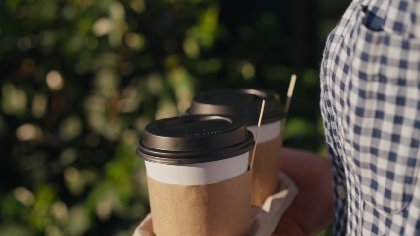 Take-away coffee. Female woman hands holding two paper cups of hot coffee in city summer park. Royalty-Free Stock Footage #1095930959