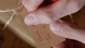 Man writing a gift tag with text FROM ME TO YOU on eco friendly wrapped gift box, close up view. - Powered by Shutterstock - Get 15% off with code: PIKWIZARD15