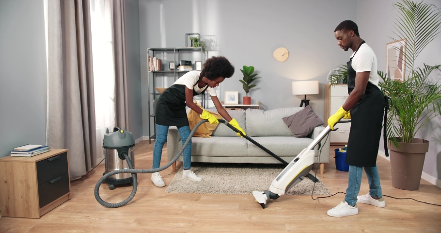 Busy African American young employees vacuuming floor with professional vacuum in living room, cleaning service, small business concept, working in apron, clean house, professional cleaner Royalty-Free Stock Footage #1095934405