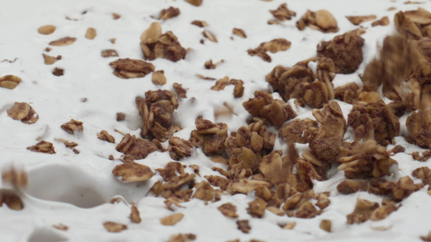 Pouring tasty granola into fresh natural yogurt in super slow motion close up. Baked oat flakes falling on creamy dessert surface. Delicious wheat ingredient for preparing nutrient breakfast. Royalty-Free Stock Footage #1095935219