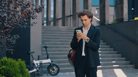 Caucasian businessman is standing near the business centre, answering on the work chats on the social media. Male boss using smartphone, texting with clients, swiping apps - Powered by Shutterstock - Get 15% off with code: PIKWIZARD15