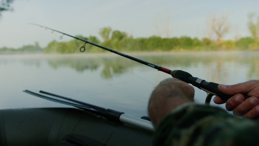 A fisherman holds a fishing rod and twists the fishing line into a reel while fishing from a boat