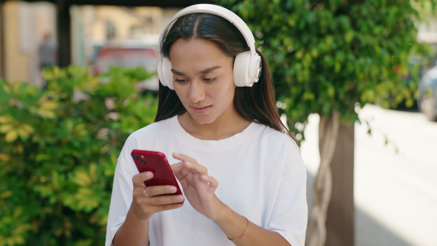 Young beautiful hispanic woman listening to music and dancing at street
