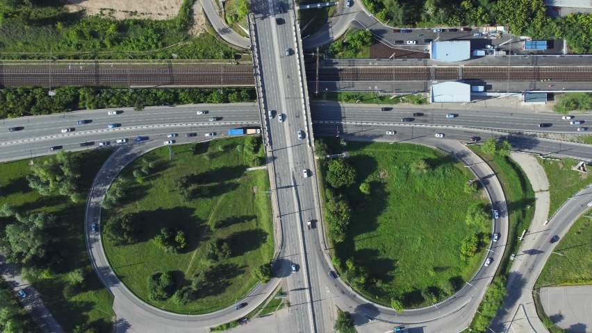 4k Above view of cars drive on roads in city on summer day irrl. Aerial of transport moving on intersecting asphalt roadways in district with green vegetation outdoors. Modern drone view of