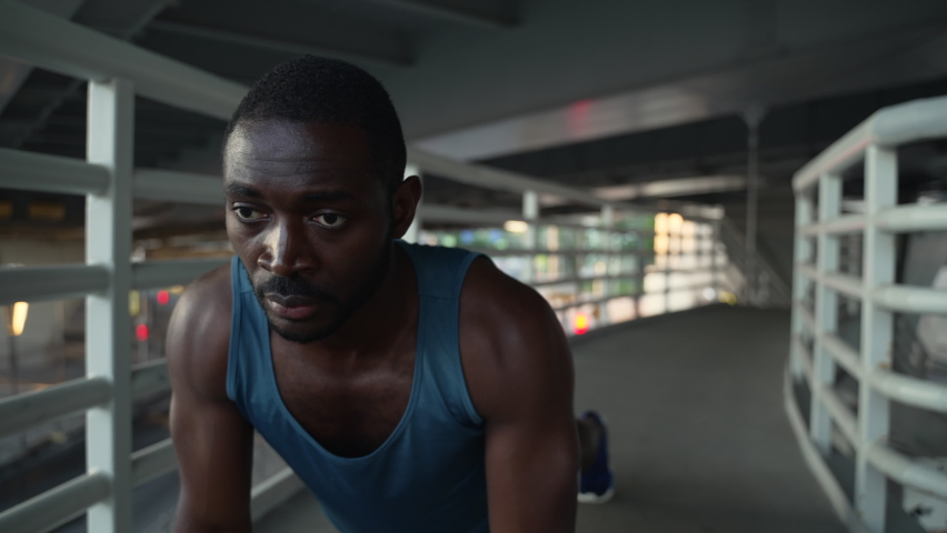 4k Young male athlete is doing push-ups and training on bridge in modern city spbas. Close view of american african man does floor exercise and trains hard, poses confidently and spends morning