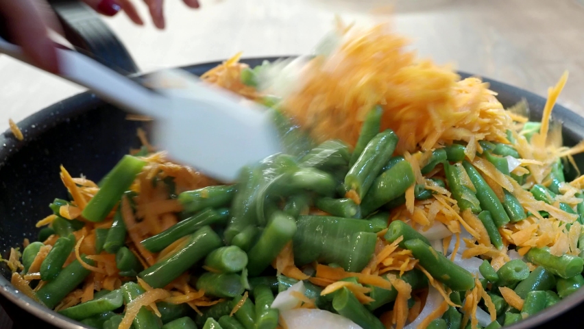 Close-up hands of a woman cooking stew green beans with carrot, onion on a fried pan at the kitchen, video 4k resolution