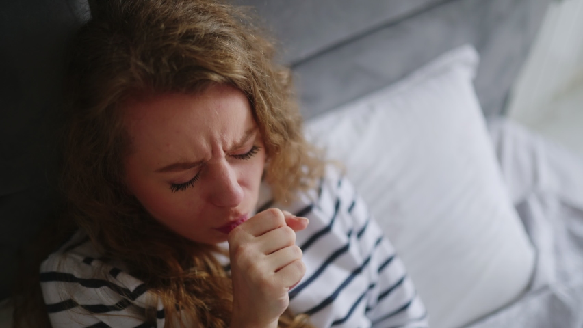 Woman sick with flu coughing and blowing her nose on her bed at home having sore throat, fever and headache. Young caucasian female suffering from coronavirus Covid19 while isolating touches forehead | Shutterstock HD Video #1095958191
