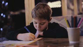 cute little boy drawing with colour pencils sitting at the table in restaurant. Video with film grain effect