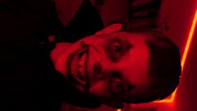 Young boy dressed in black and looking scary, dancing and doing funny faces, red light on the background, halloween time concept, vertical video