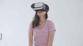 Young asian woman wearing vr headset playing game with excited on bed in the bedroom at home, female using virtual reality or metaverse innovation for simulation 3D, lifestyles and technology concept.