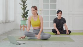 Young woman and asian man doing yoga with sitting and stretch muscles back and hands on mat at home, couple training practicing workout with exercise while watching laptop computer, sport concept.