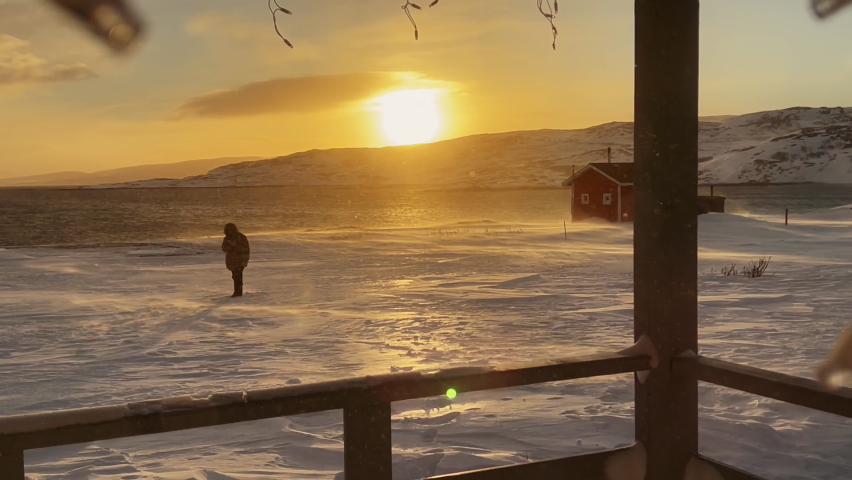 from the first person. View from the porch of a wooden house in winter. Beautiful winter sunset in Siberia. The snow is falling and the sun is shining. 