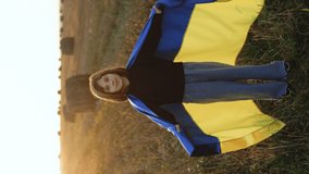 Vertical video of young girl with blue and yellow ukrainian flag. Stop war in Ukraine. Russia stop war. Kid standing outdoors at sunset. International day of democracy concept. Flag Day.