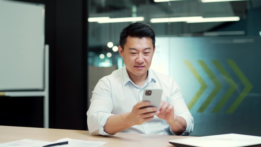 Happy asian man employee enjoys success read good news in smartphone. businessman win mobile online bet bid money financial prize victory receive offer opportunity on smart phone in the office indoor Royalty-Free Stock Footage #1095968041