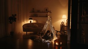 Dad and little son holding flashlights, reading book, chatting and laughing while he lying in teepee tent decorated with lights in dark room in the evening - Powered by Shutterstock - Get 15% off with code: PIKWIZARD15