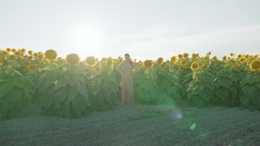Beautiful young girl in elegant dress among sunflowers under summer sun