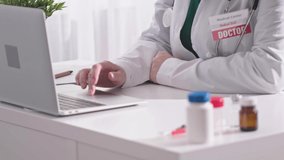 doctor table workplace female doctor's hands working laptop white table pills bottles on desk red medicine badge on white coat. working doctor concept