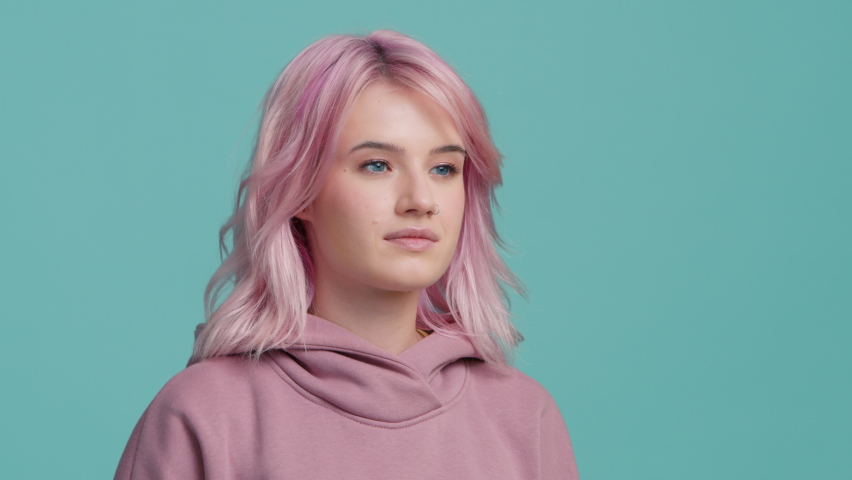 Silence gesture young Hipster girl with pink hair showing index finger to lips. Serious model with trendy hair color makes gesture for silence, looking at camera on blue background. Don't tell gesture Royalty-Free Stock Footage #1095976947
