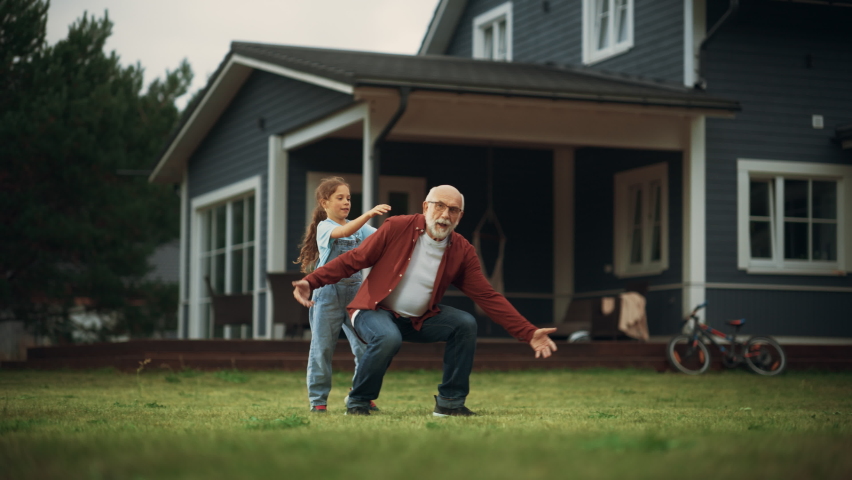 Happy Granddad Enjoying Time Outdoors with His Grandchild, Playing with Energetic Young Girl. Joyful Grandpa Giving a Piggyback Ride on a Lawn in Front of the House. Royalty-Free Stock Footage #1095980887