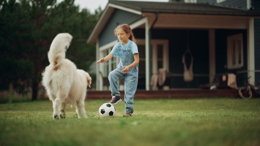 Young Girl Enjoying Time Outside with a Pet Dog, Playing Ball with an Energetic White Golden Retriever. Happy Young Kid Playing Football with a Dog on a Lawn on Front Yard at Home.