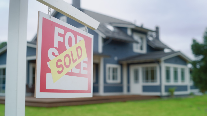 Close Up of a House Sold Sign on a Lawn in Front of a Big Modern House with Traditional Architecture. Housing Market Concept with Residential Property in the Countryside.