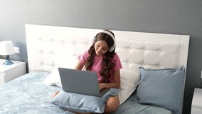 happy little girl in headphones using smartphone and laptop for online education, home schooling