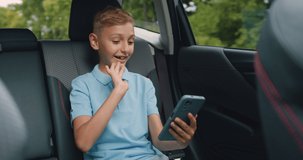 Good-looking smiling happy boy-teenager sitting on car's rear seat and has video call on phone during trip