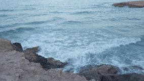Waves crashing on the rocks at the beach in La Zenia in Spain. The water has a beautiful light blue color. It is a beautiful summer evening. Video to symbolize strong current or just holiday