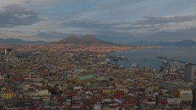 Aerial panoramic footage of city at sunset. Majestic Mount Vesuvius lit by low sun in distance. Naples, Italy