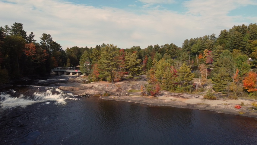 Cinematic footage of water flowing on rocks between two lakes in autumn landscape. Water surface surrounded by trees. Muskoka Region, Algonquin Provincial Park in Ontario, Canada