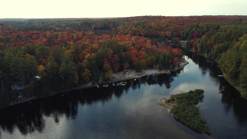 Forwards fly above calm water surface reflecting sky with clouds. Lake in colourful autumn landscape. Muskoka Region, Algonquin Provincial Park in Ontario, Canada