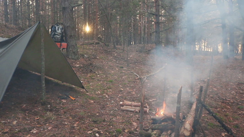 A prepper cooks food on an open fire. The action takes place in the wilderness of a wild forest.