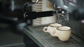 Close-up of espresso being poured into cups from a coffee machine. A slow-motion video of the process of making an Americano in a cafe. A professional barista is working. High quality 4k footage