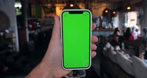 Man holding smartphone with green screen chroma key indoors at cafe or restaurant background, close-up.