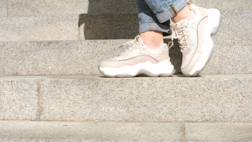 Female legs in running shoes close-up on the background of the gray stairs.