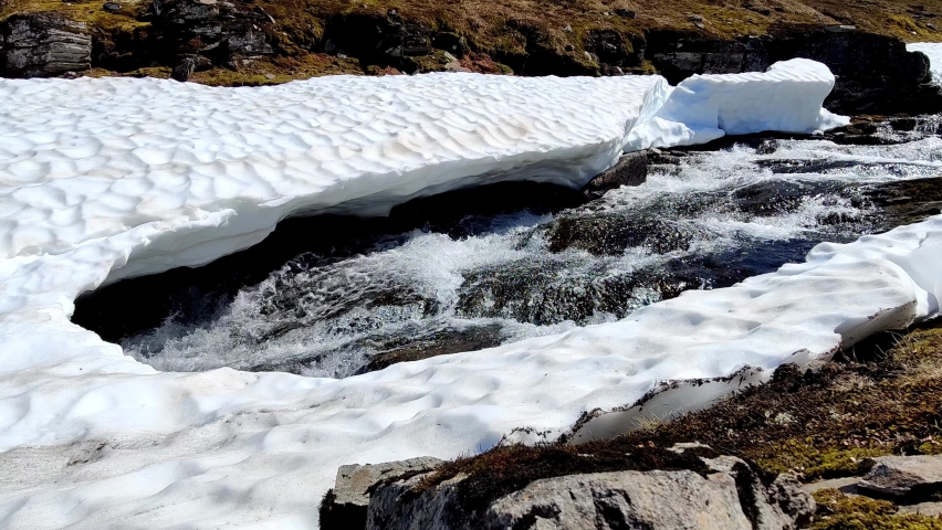 Cold fresh glacial river flowing below melted snow and ice sheet at Greenland north of polar circle - Static closeup from edge of Greenland ice sheet melting