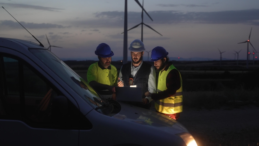 Team of technicians and engineer working in wind turbine farm at night, planing renewable energy ecology project