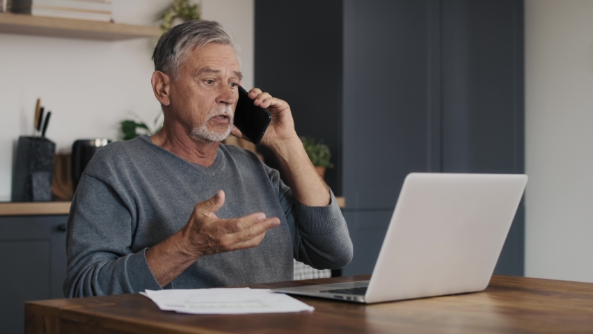 Shocked caucasian senior man looking at laptop and having phone call. Shot with RED helium camera in 8K.   Royalty-Free Stock Footage #1096029837