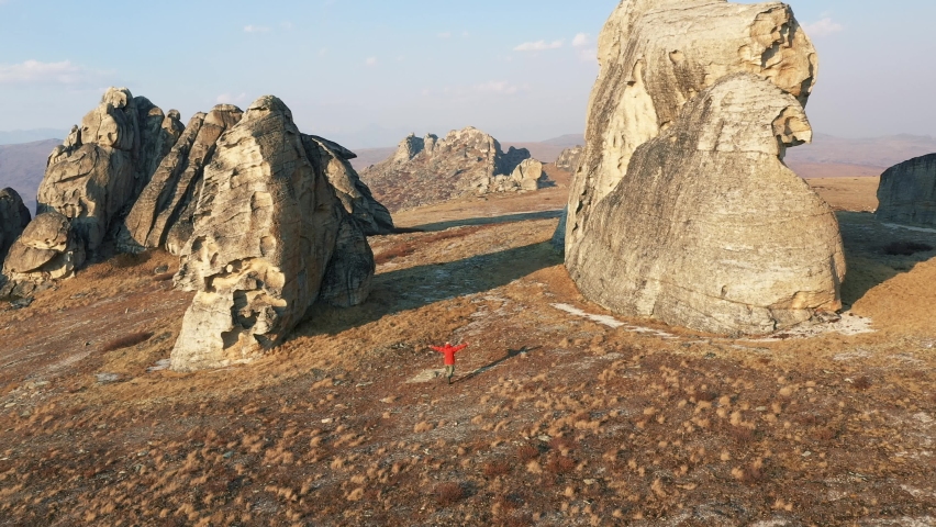 Aerial view of happy hipster tourist running along valley with his hands raised to side enjoying freedom showing flight. Against troll fingers rocky remnants shape of monolithic tower in national park