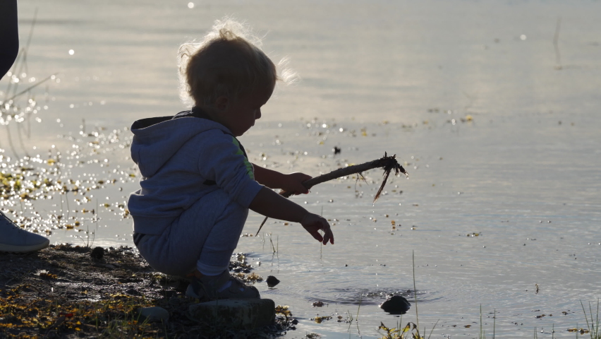 Silhouette of mother with toddler child on the shore of the lake on a summer evening at sunset. Simferopol, Crimea.