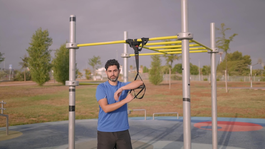 Portrait of confident caucasian man exercising outside in sunny park. Great TRX workout. Young handsome guy in sportswear doing exercising outdoors. Healthy lifestyle concept.