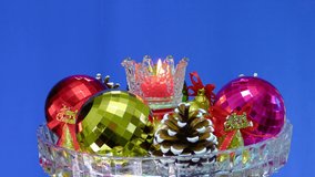 Christmas decorations and a burning candle rotate in a glass flask on a blue background