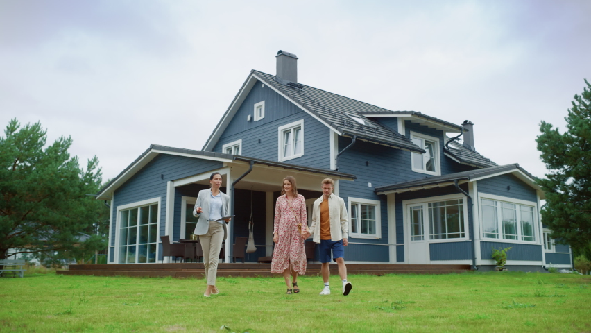 Real Estate Agent Showing a Beautiful House to a Young Happy Couple. People Walking Outside on a Lawn, Talking with Businesswoman, Discussing Buying a New Home. For Sale Sign on the Street. Royalty-Free Stock Footage #1096061519