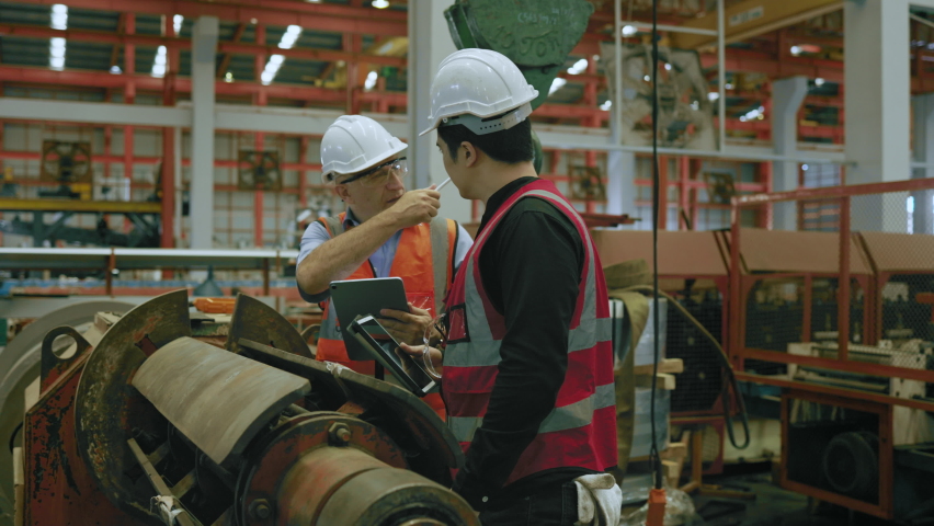 Two engineers, one with a clipboard, engage in a serious discussion over machinery in a busy factory setting, showcasing teamwork and problem-solving in industrial operations Royalty-Free Stock Footage #1096071419