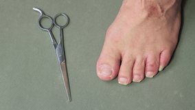 A hand with metal scissors cuts the nail of a toe of a male foot. The concept of male pedicure and foot care. Isolated video, copy space, close-up. UHD 4K.