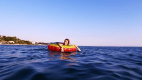 A woman swims in an inflatable bright life buoy in the blue sea enjoying the summer sun. Sea relaxation.