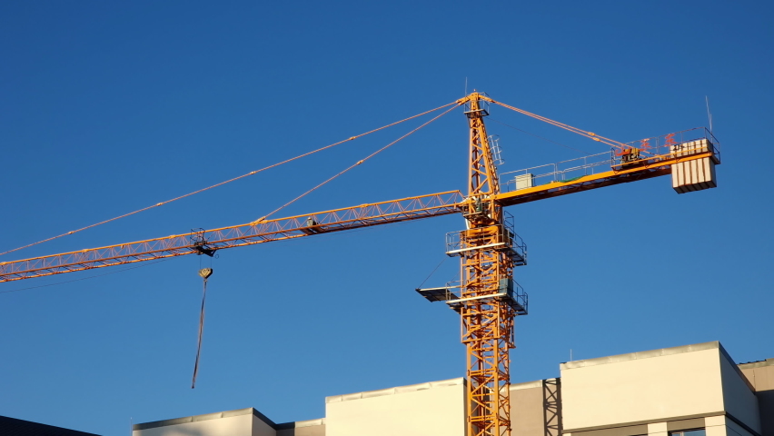 Yellow tower crane on a construction site, against clear blue sky, illuminated by late afternoon sun.