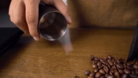Metal cup scoops coffee beans close up. Tracking shot of barista hand holding metal cup gathering brown fresh seeds on wooden table in slow motion. - Powered by Shutterstock - Get 15% off with code: PIKWIZARD15